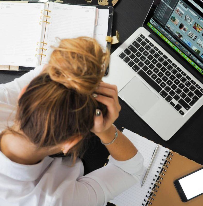 Depressed girl sitting next to laptop with hand on her head