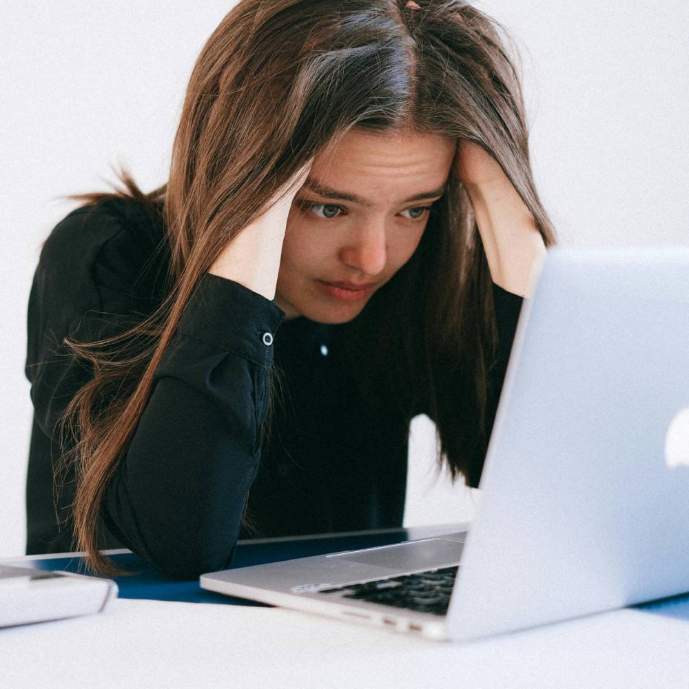 a woman sitting in front of a laptop with her head in her hands